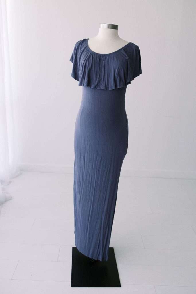 Mannequin displaying a floor-length, short-sleeve, blue dress with a ruffled neckline in a minimalist, white room.