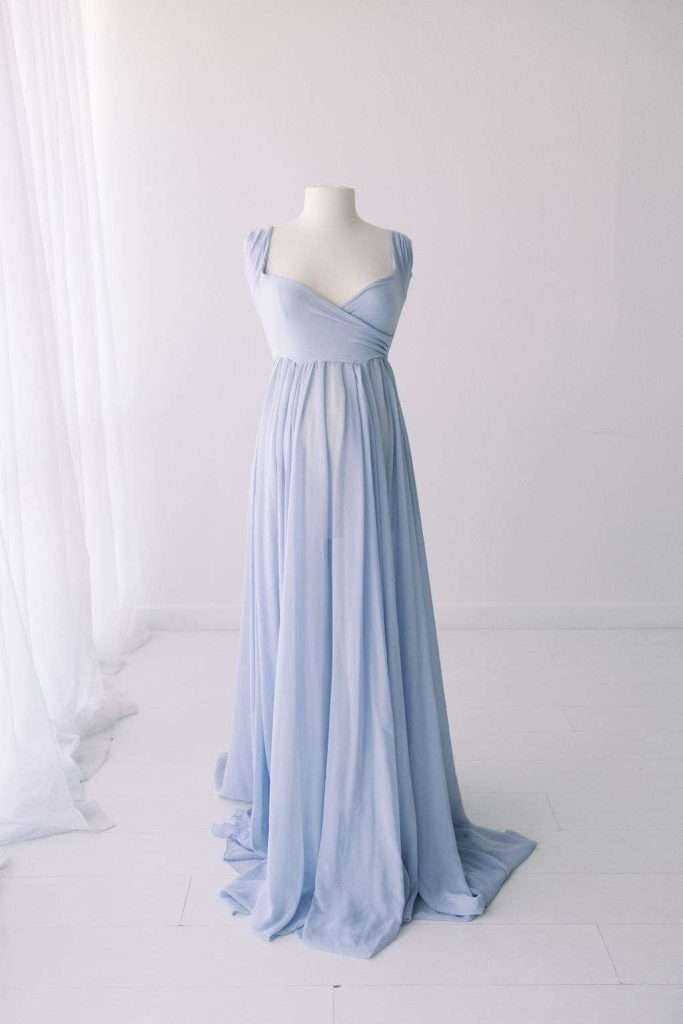 A light blue, floor-length gown with a fitted bodice and flowing skirt displayed on a white dress form in a minimalist room.