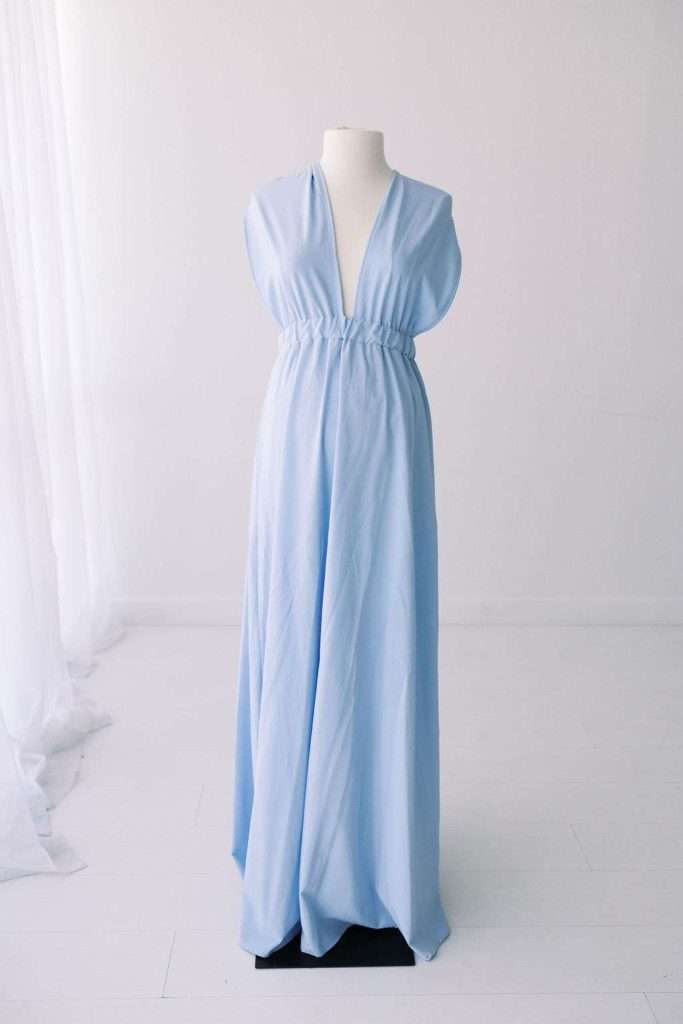 Sleeveless light blue floor-length dress with a deep V-neck and gathered waist, displayed on a white mannequin in a minimalist, white room.