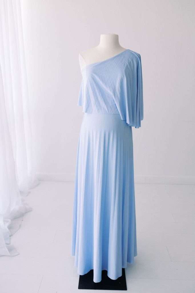 Mannequin dressed in a light blue, one-shoulder, floor-length gown with a draped sleeve and fitted waist, set against a plain white background.