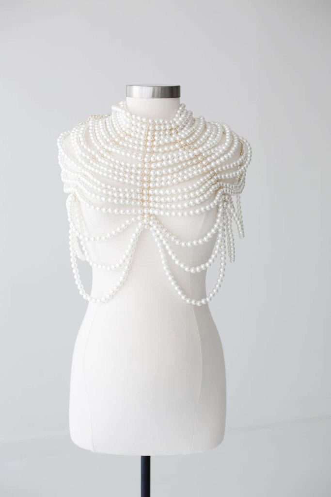 A mannequin displays an elaborate pearl necklace draped over the shoulders and chest against a plain, light background.