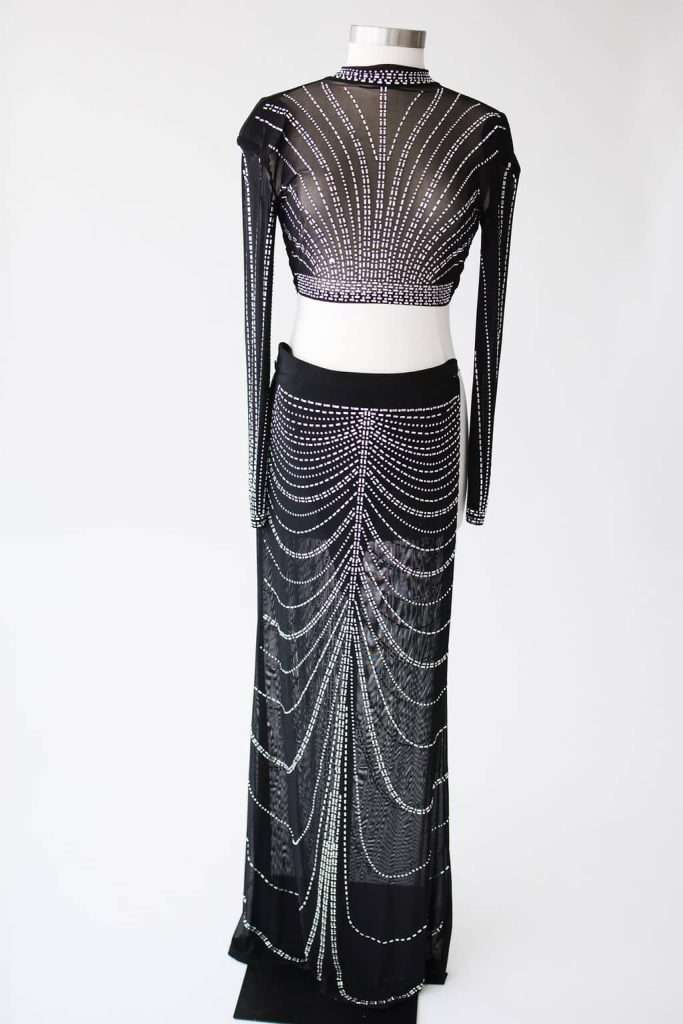 Black sheer two-piece outfit with long sleeves and high neckline, featuring symmetrical silver bead or rhinestone patterns, displayed on a dress form against a white background.