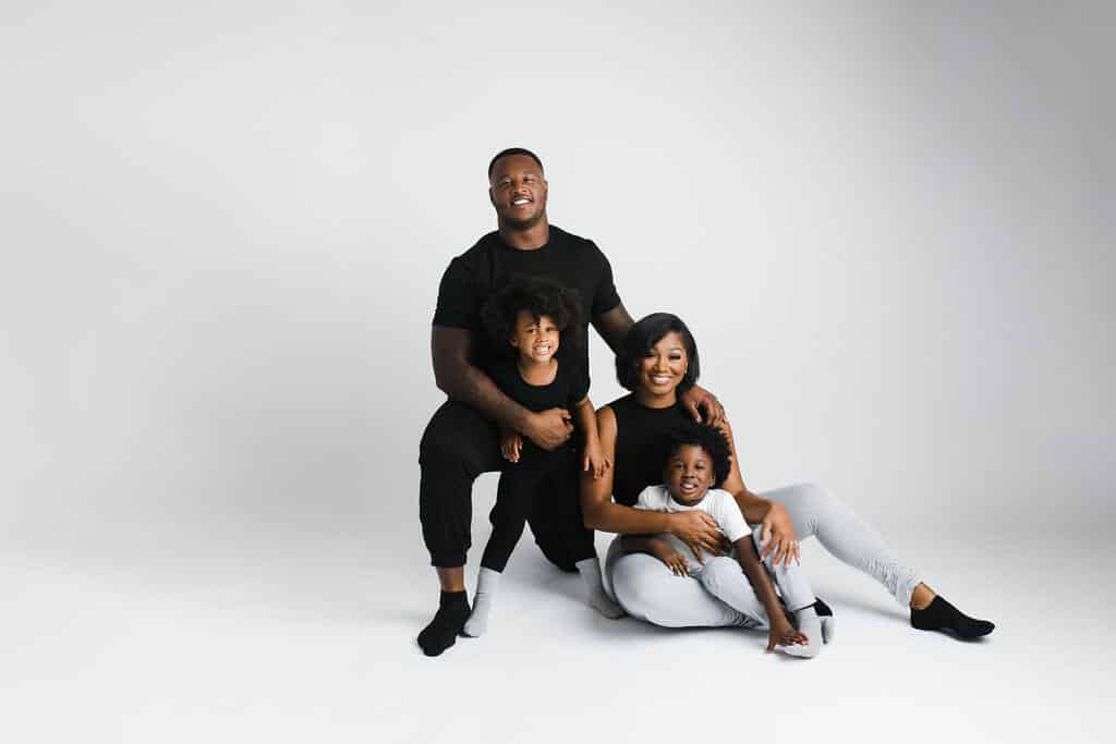 A family of four poses in a studio against a white background, with two adults and two children sitting and smiling at the camera.