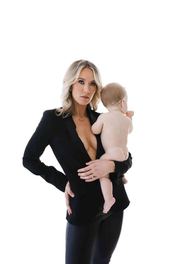 Woman in a black blazer holding a naked baby against a plain white background.