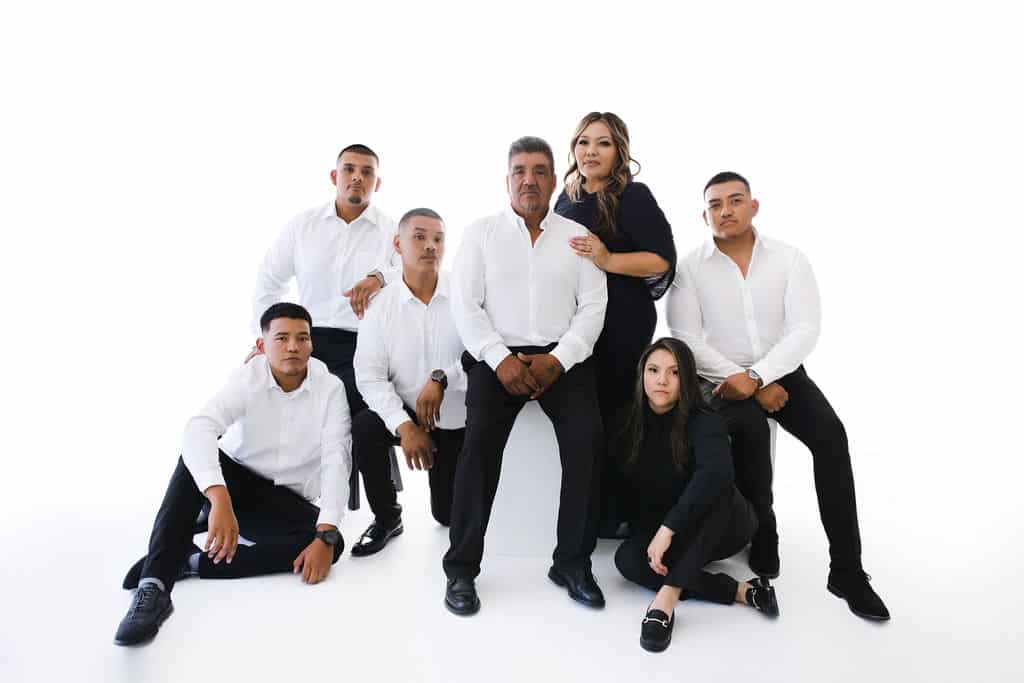 Seven people pose for a family portrait against a white background, wearing coordinated black and white outfits.