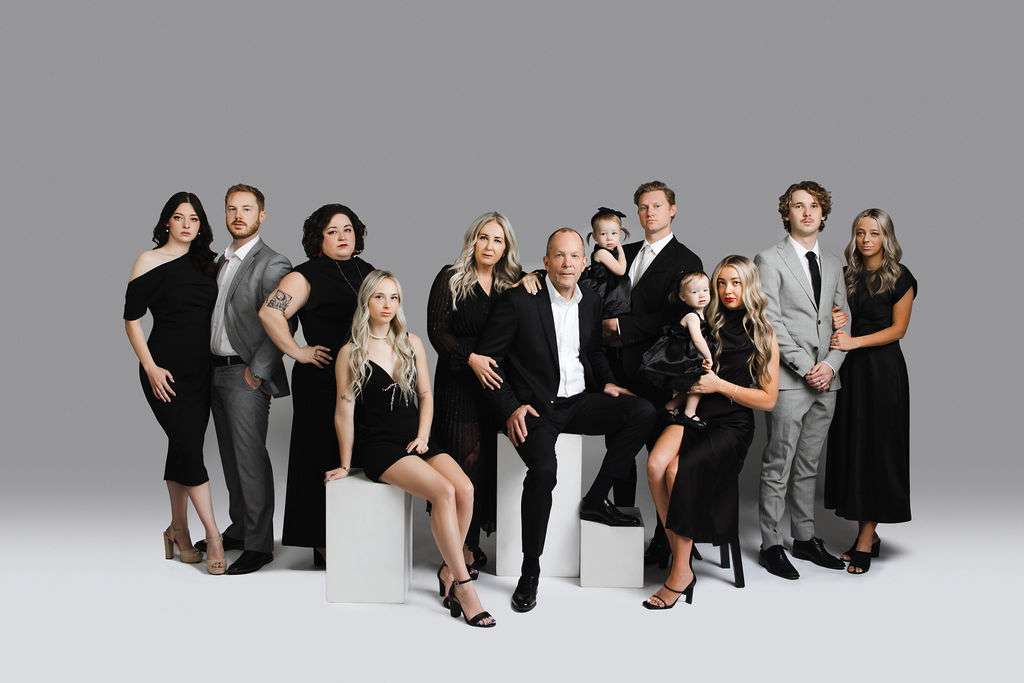 Eleven adults and one child, all dressed in formal black and gray outfits, pose together against a plain gray background.