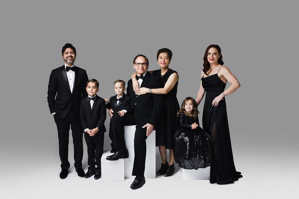 Six people, including two children, pose for a formal family portrait wearing black evening attire against a plain gray background.
