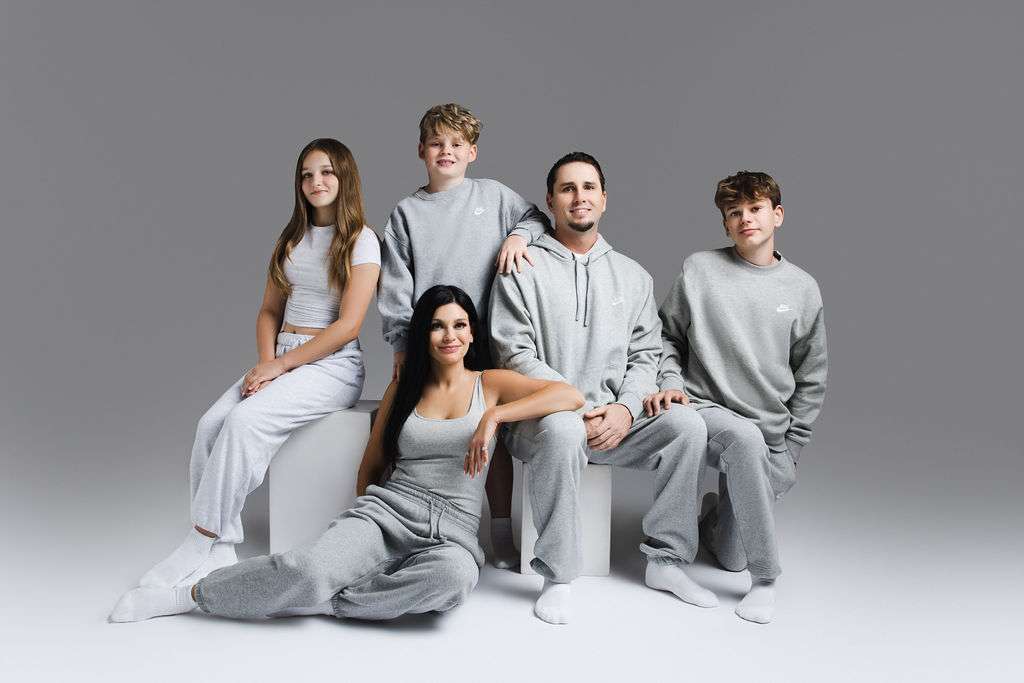 Five people pose together in coordinated grey and white loungewear against a plain grey background, sitting and standing around white cubes.