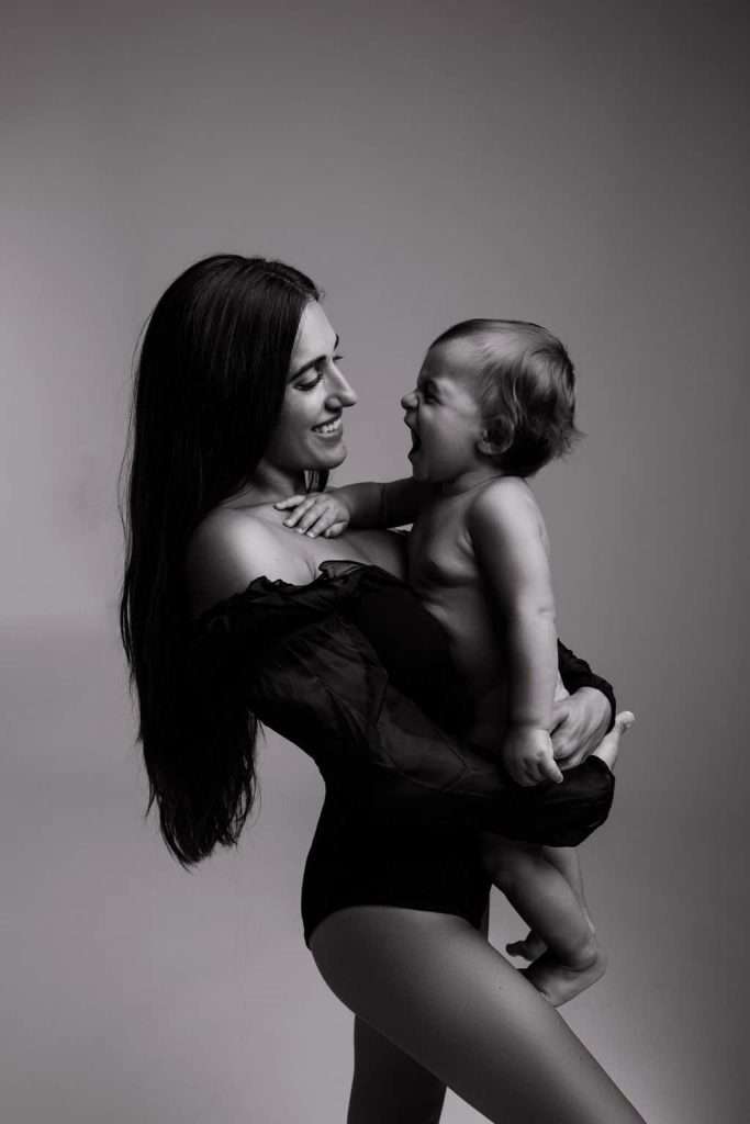 A woman holds a laughing baby in her arms. Both are looking at each other, and the photo is in black and white.