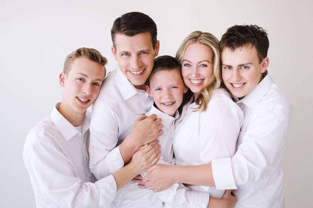 Five people, all wearing white shirts, stand close together and smile at the camera against a plain white background.