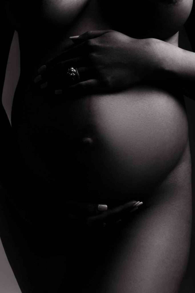 A close-up, black and white photo of a pregnant woman’s bare belly, with hands gently resting above and below it.