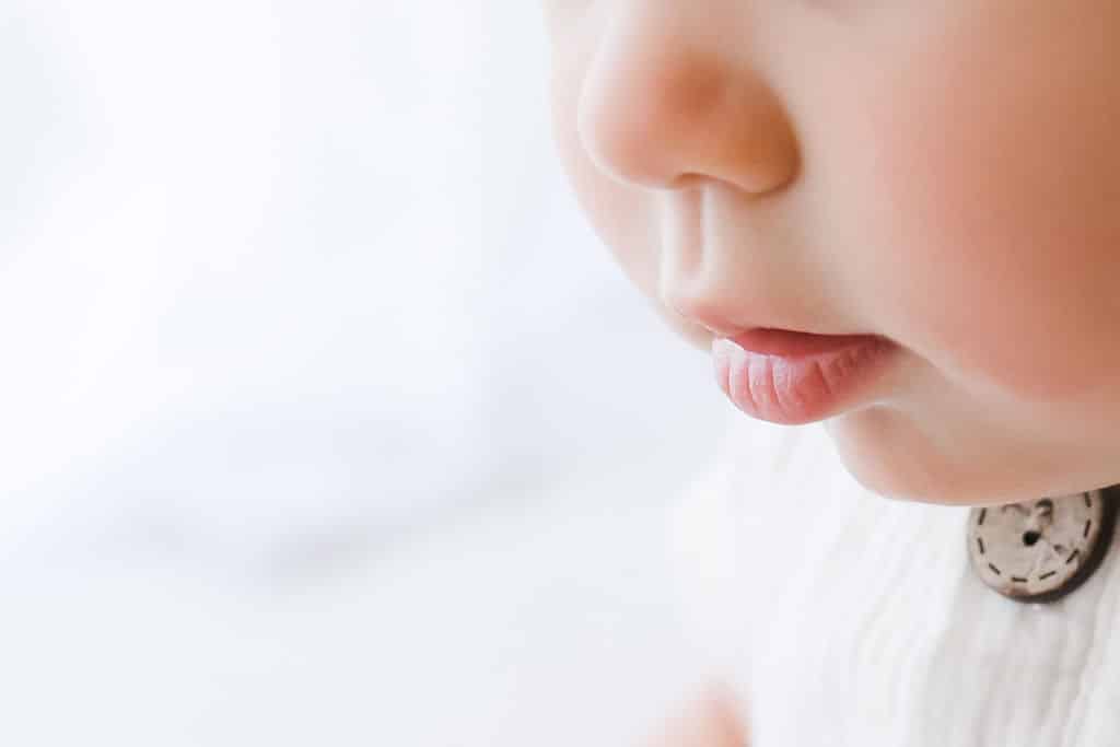 Close-up of a baby’s face focusing on the nose, lips, and part of the cheek, with soft lighting and neutral background.
