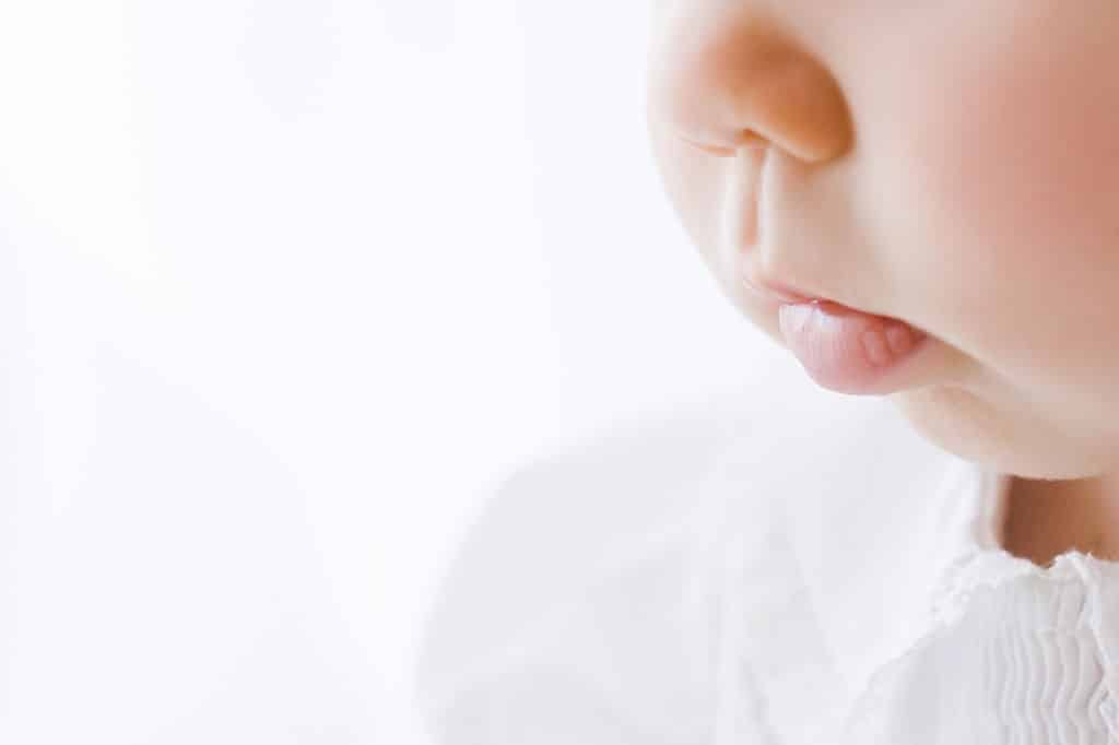 Close-up of a baby’s face, focusing on the lips, nose, and cheek, with a soft white background and white clothing visible.