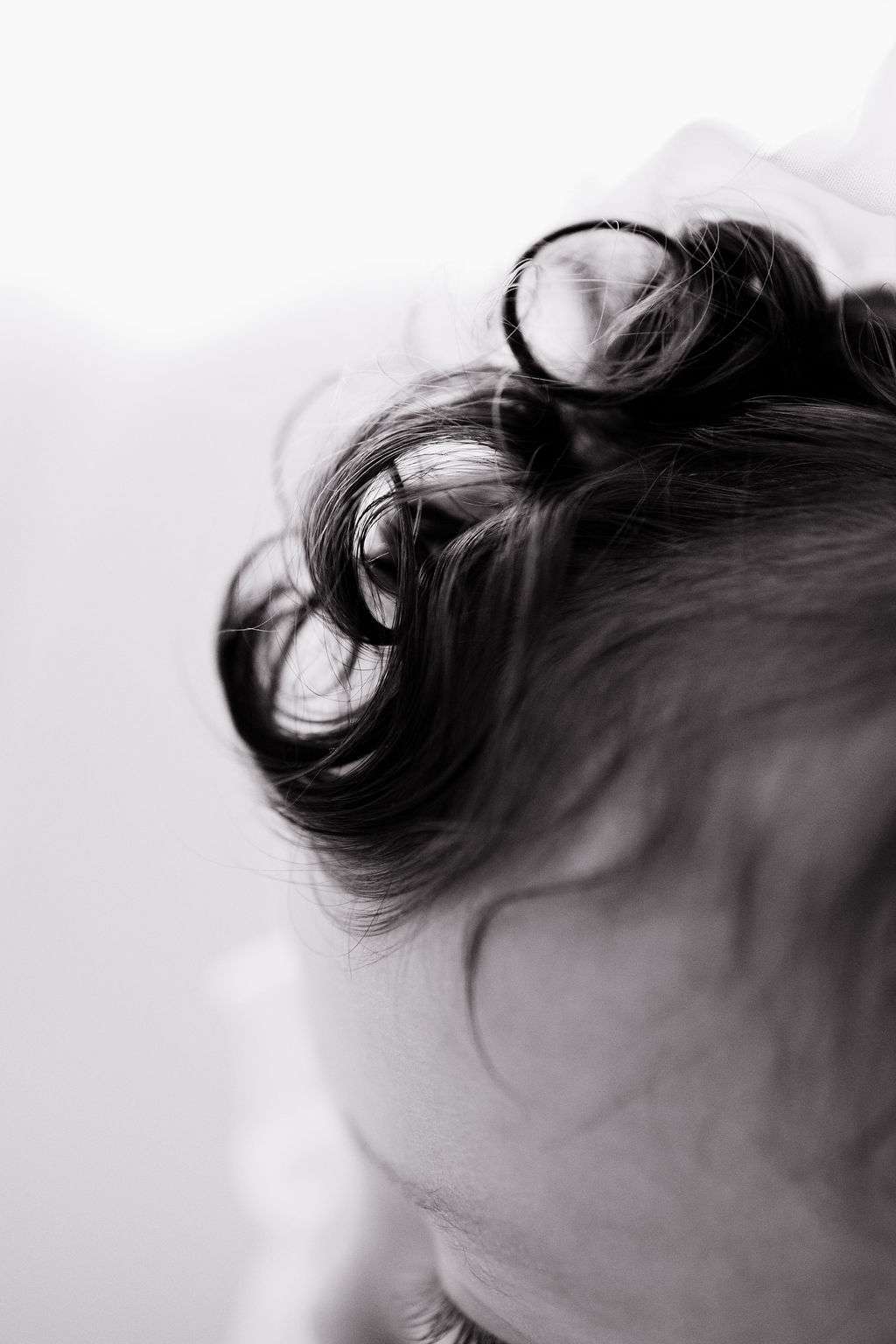 Close-up of a child’s head with soft curls of hair in focus; image is black and white with a blurred background.