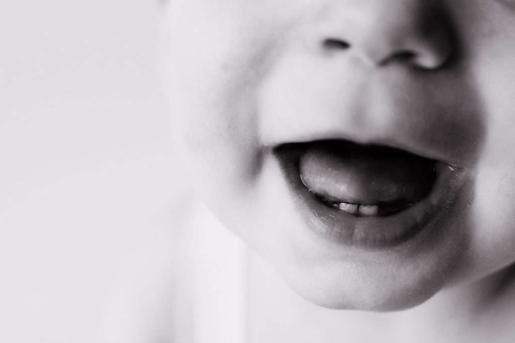 Close-up black and white photo of a baby’s mouth, showing their lips slightly open with two visible baby teeth on the lower gum.
