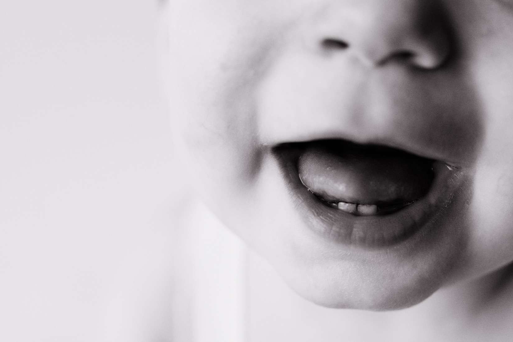 Close-up black and white photo of a baby’s mouth, showing their lips slightly open with two visible baby teeth on the lower gum.