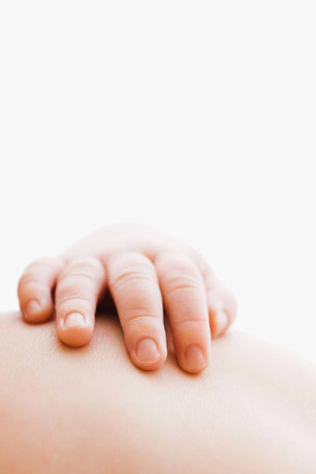 A baby’s hand rests gently on an adult’s skin against a white background.