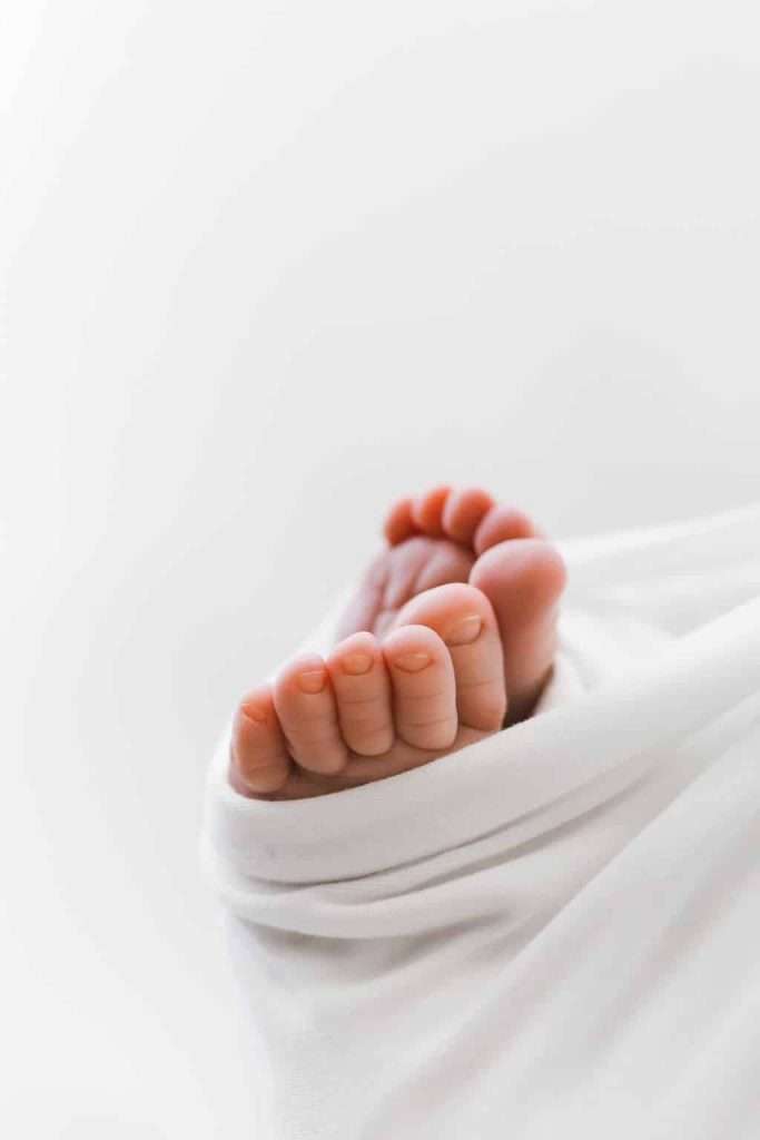 Close-up of a baby's bare feet wrapped in a soft white blanket against a plain light background.