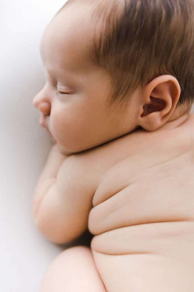 A close-up side view of a sleeping baby lying on their stomach, showing the baby's back, head, and soft skin folds.
