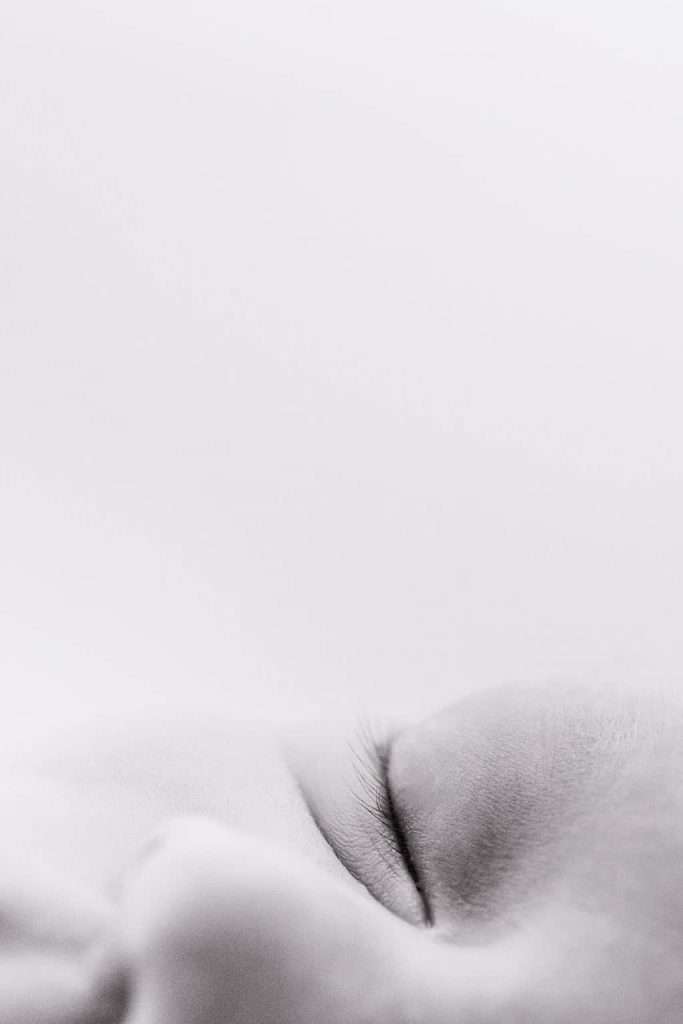 Close-up, black-and-white image showing the closed eye and part of the face of a person, with a soft focus and minimal background.