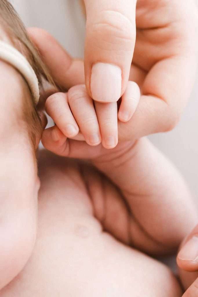 Adult hand gently holding a newborn baby's hand, showing a close-up of their fingers touching.