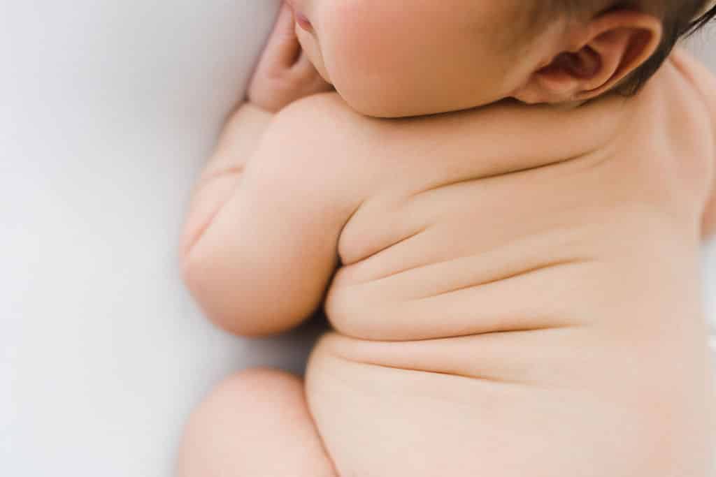 Close-up of a baby lying on their side, showing soft skin and natural rolls, with the baby's face partially out of frame.