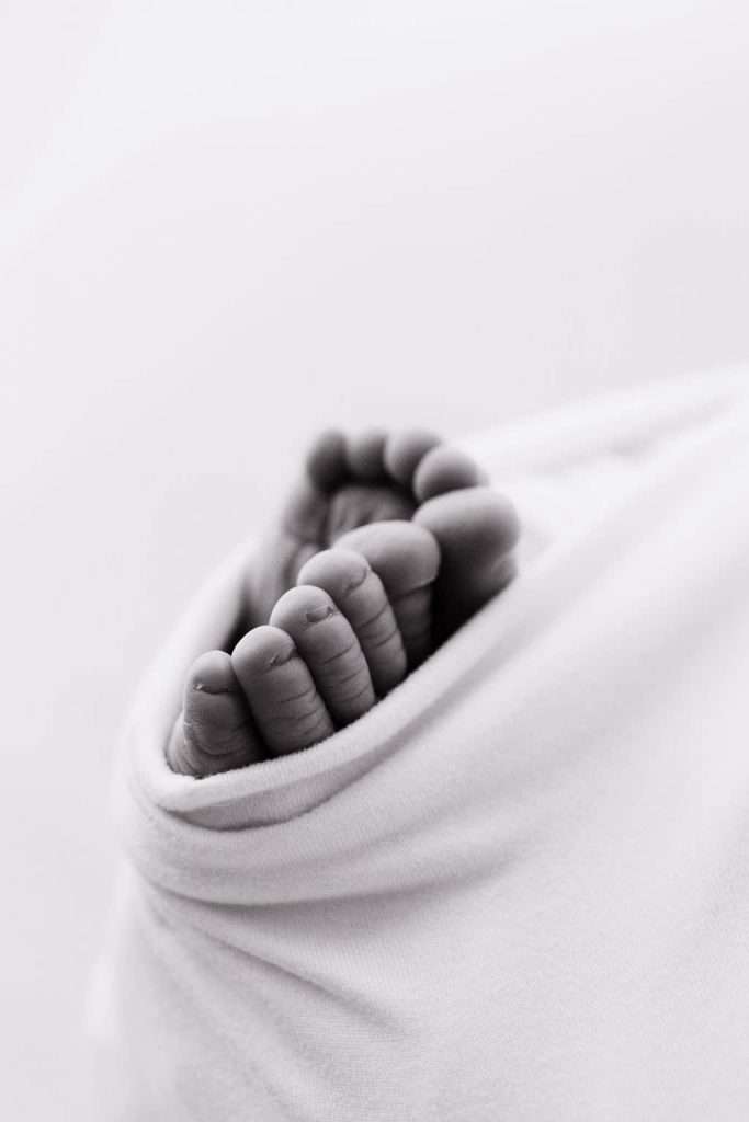 Close-up of a baby's feet wrapped in a soft white blanket, shown in black and white.