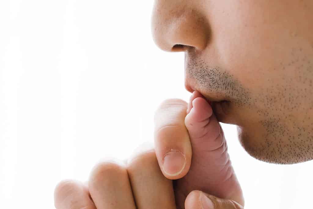 Close-up of an adult gently kissing a newborn baby's hand against a white background.