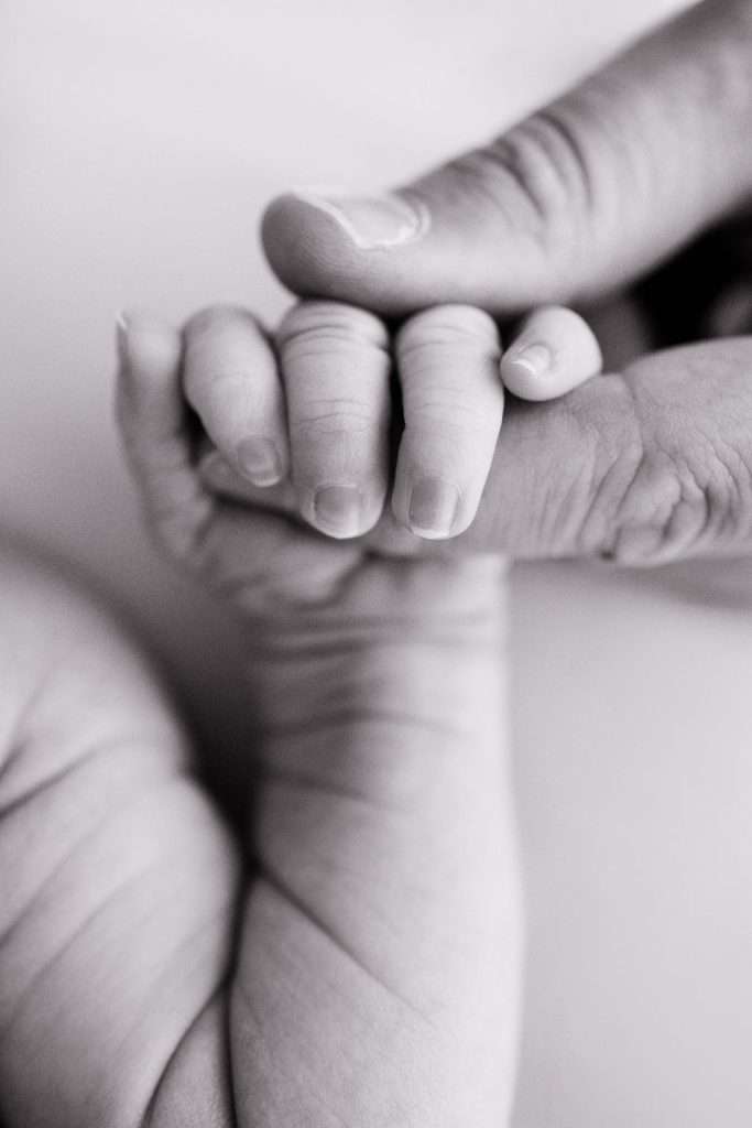 A close-up of a baby's hand gripping an adult's finger, with both hands shown in black and white.