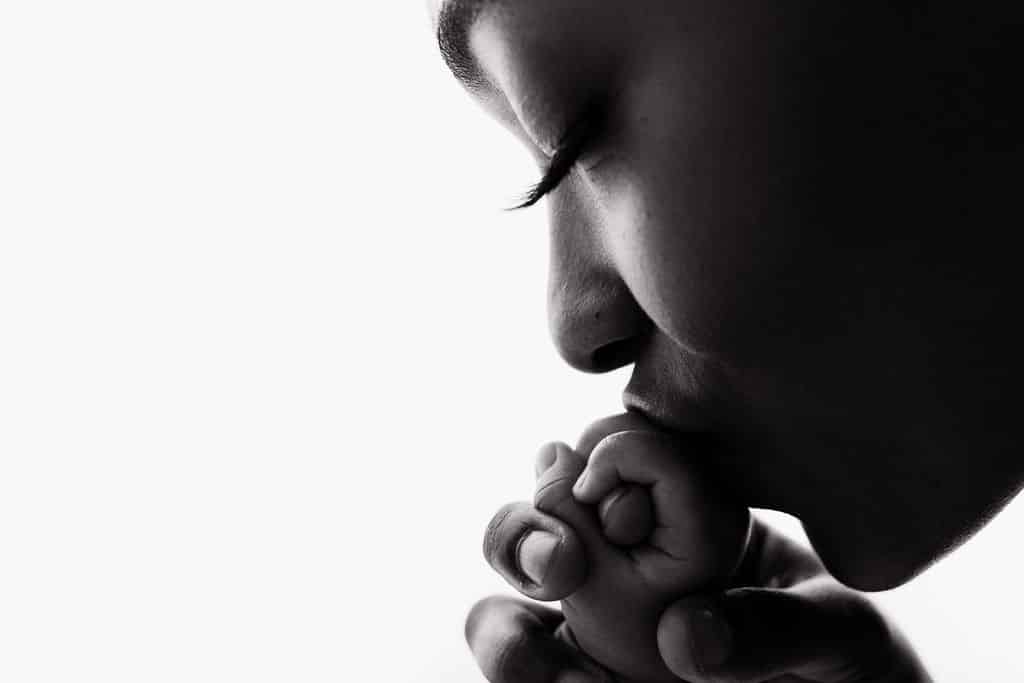 Close-up of an adult gently kissing a baby's hand, showing a tender moment of affection against a white background.