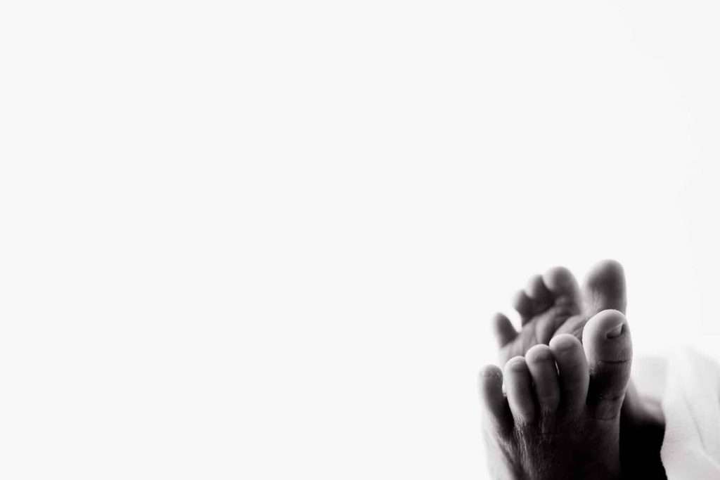 Close-up of two feet resting against a white background, positioned in the lower right corner of the image.