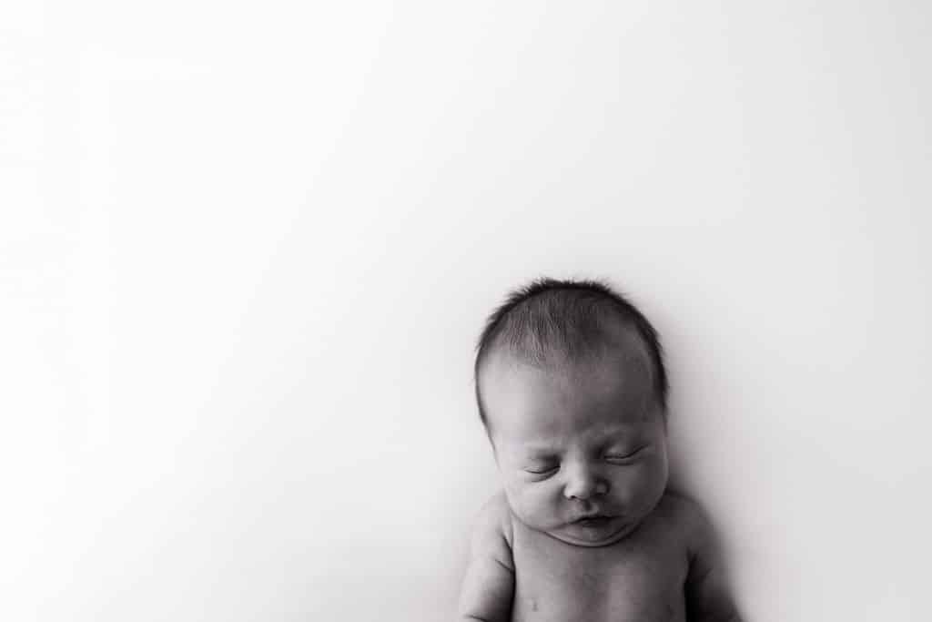 Black and white photo of a newborn baby with closed eyes, positioned at the bottom right of a mostly white background.