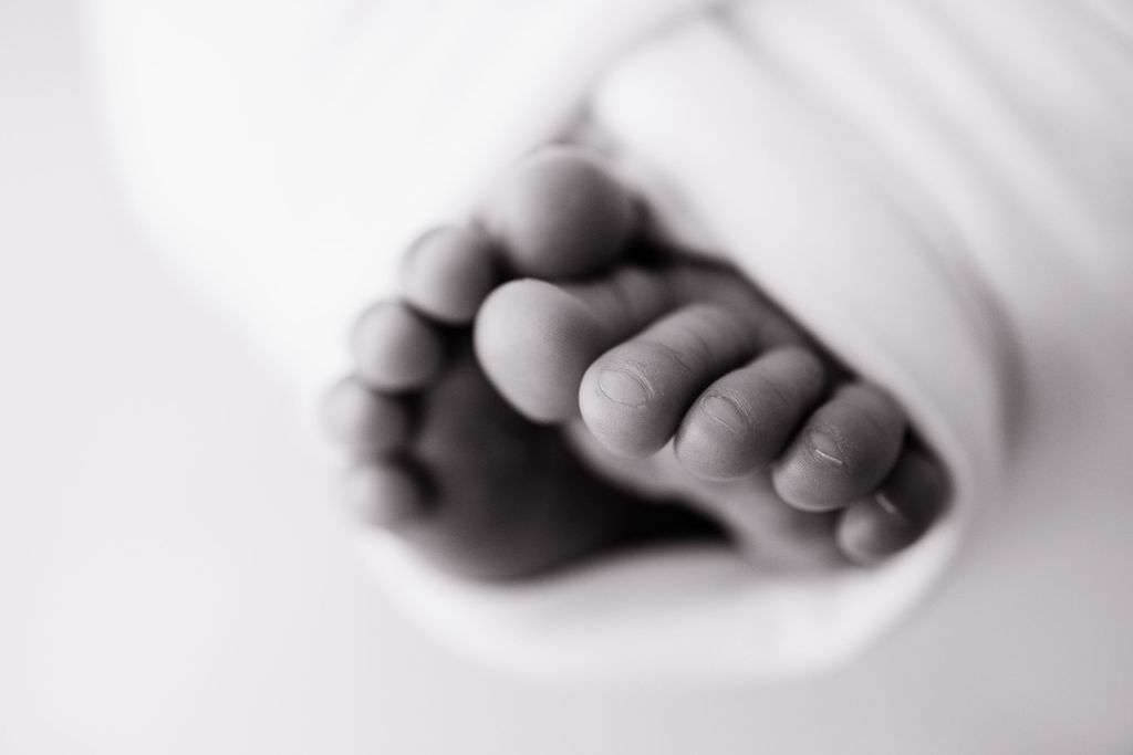 Close-up of a baby's feet wrapped in a soft white blanket, with focus on the toes and a blurred background.