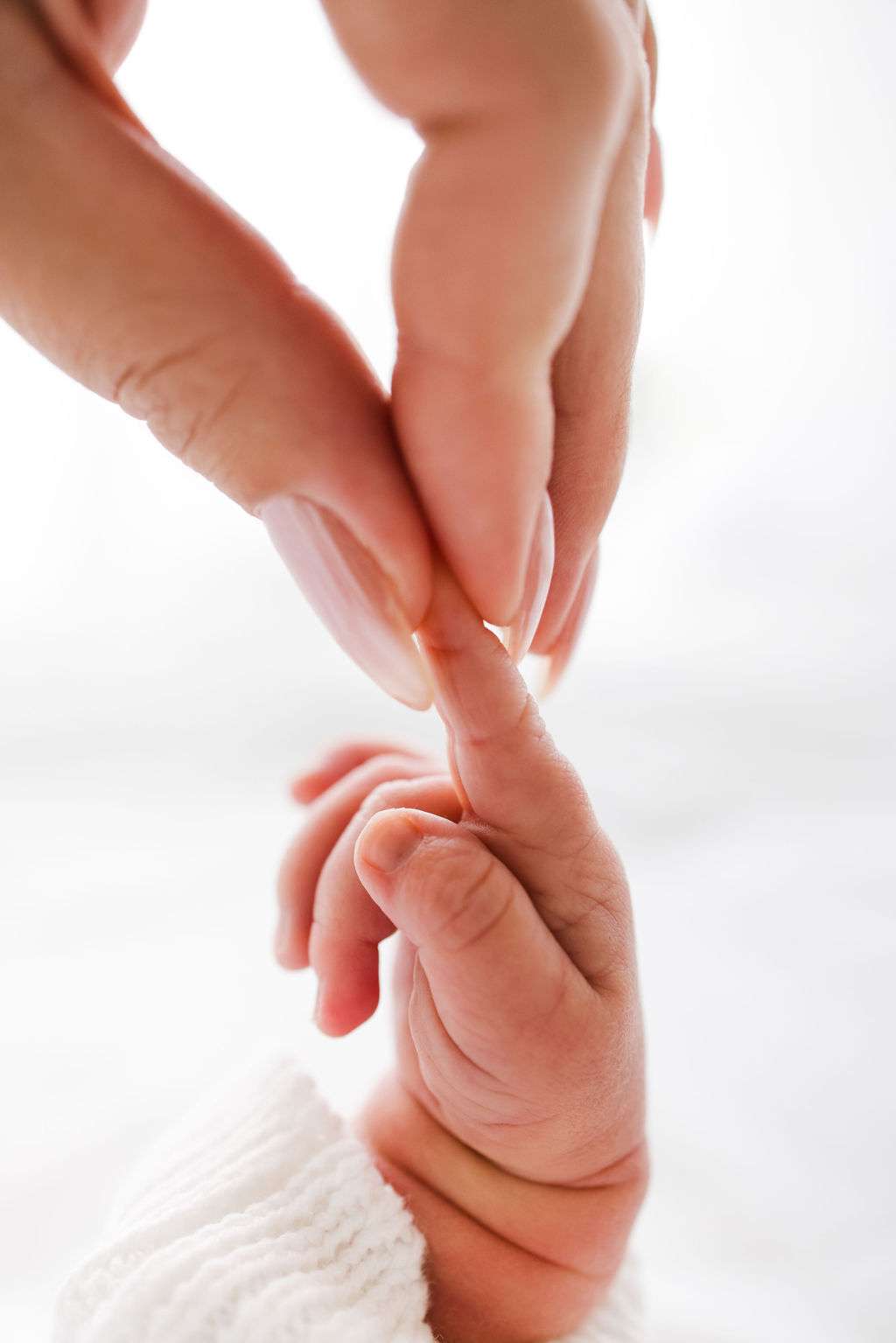 Close-up of an adult hand gently holding a newborn baby's fingers against a soft, light background.